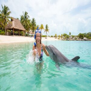 Mulher sorrindo nadando ao lado de um golfinho em lagoa turquesa perto de Cancún